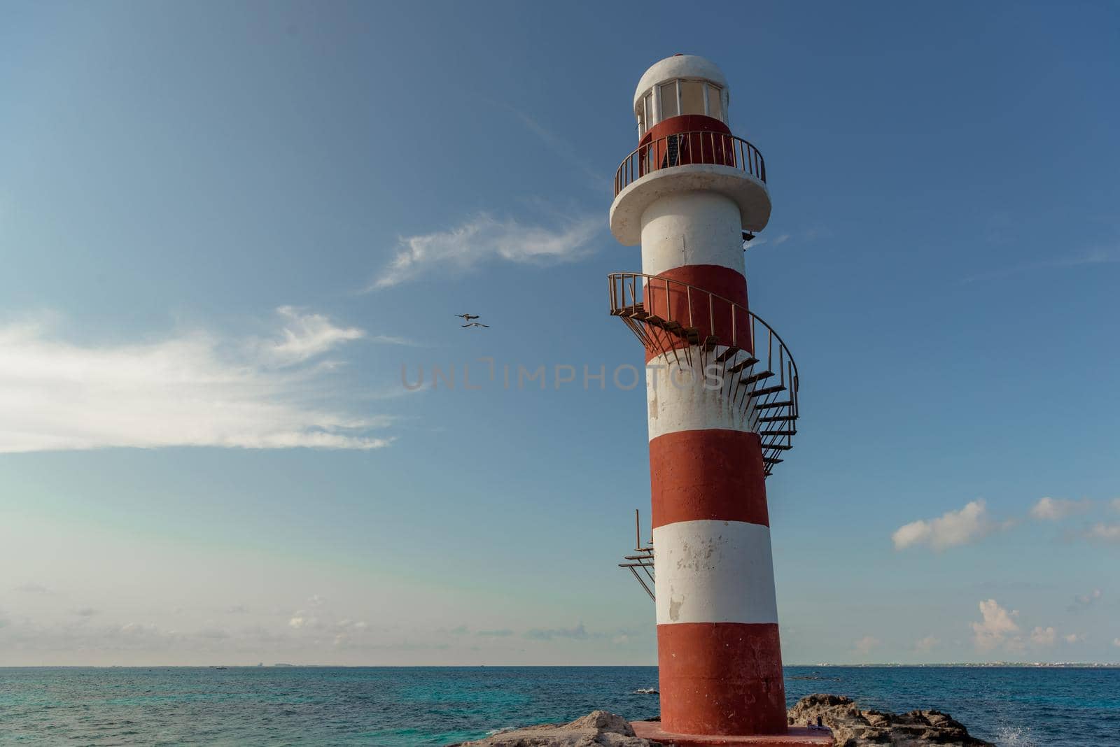 Top of a white-red lighthouse against a blue sky with an airplane. Mexico.