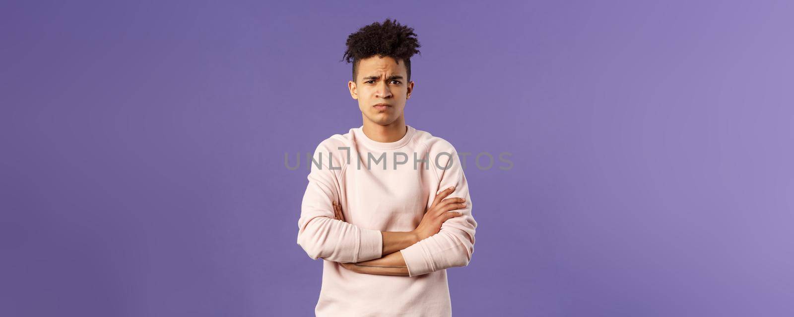 Portrait of young offended hispanic boyfriend, frowning and looking judgemental upset at camera, cross hands over chest defensive insulted pose, standing purple background angry at someone.