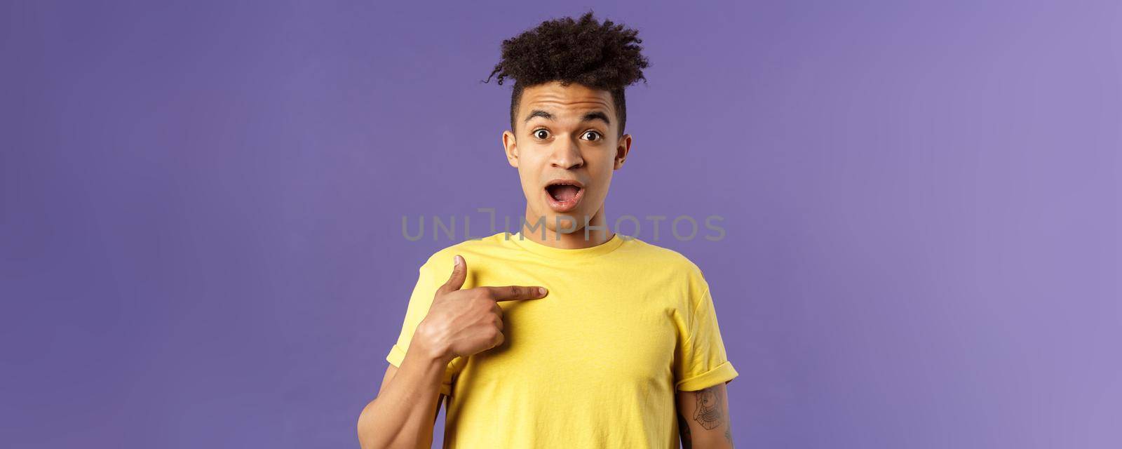Who me, no way. Portrait of surprised, happy rejoicing young man looking with disbelies as being chosen from all candidates, pointing at himself open mouth fascinated, purple background.