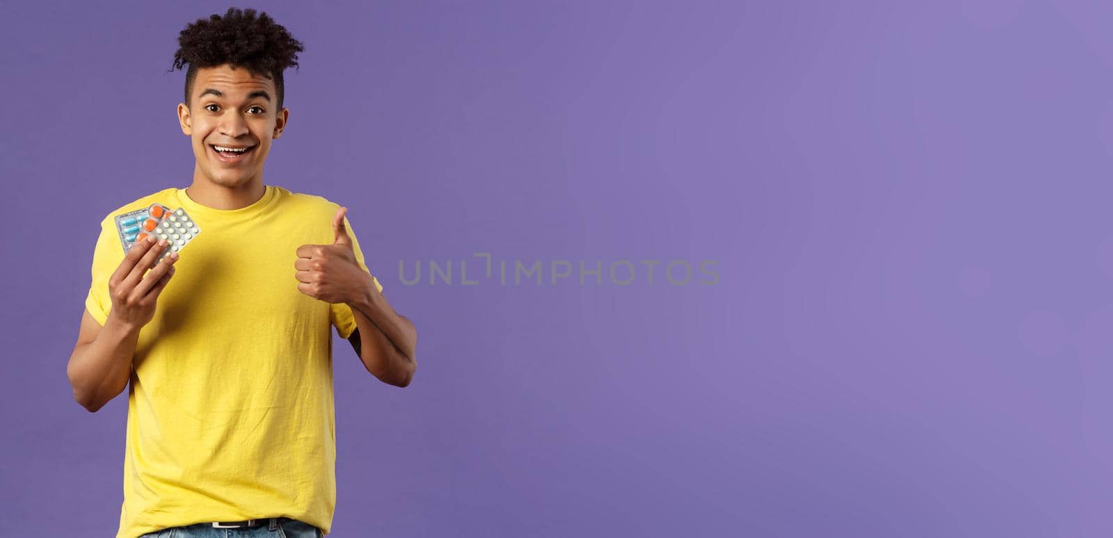 Health, influenza, covid-19 concept. Portrait of young healthy man got better, show thumbs-up holding drugs, taking pills to feel better after catching cold, being sick, purple background by Benzoix