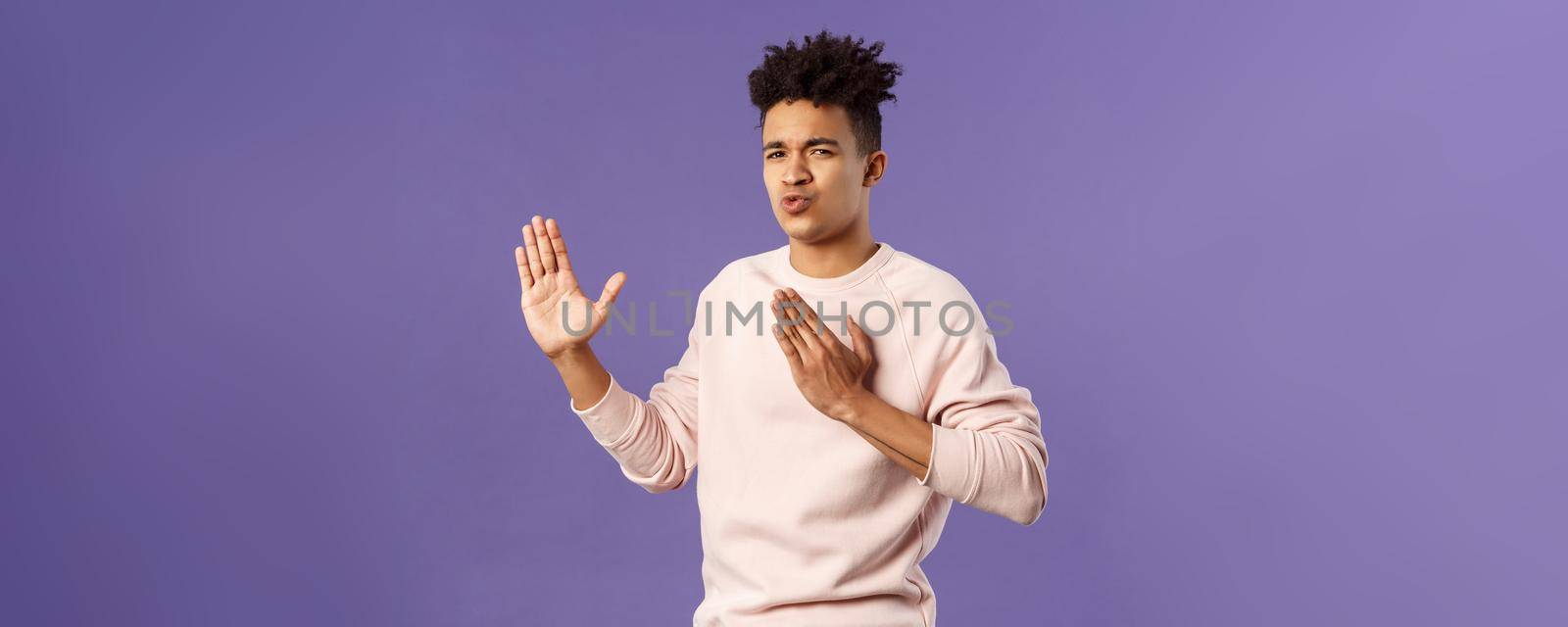 Portrait of funny and carefree young hispanic guy holding hands in martial arts attack pose, folding lips acting sassy and cool as imitating ninja, ready to defeat coronavirus, purple background.