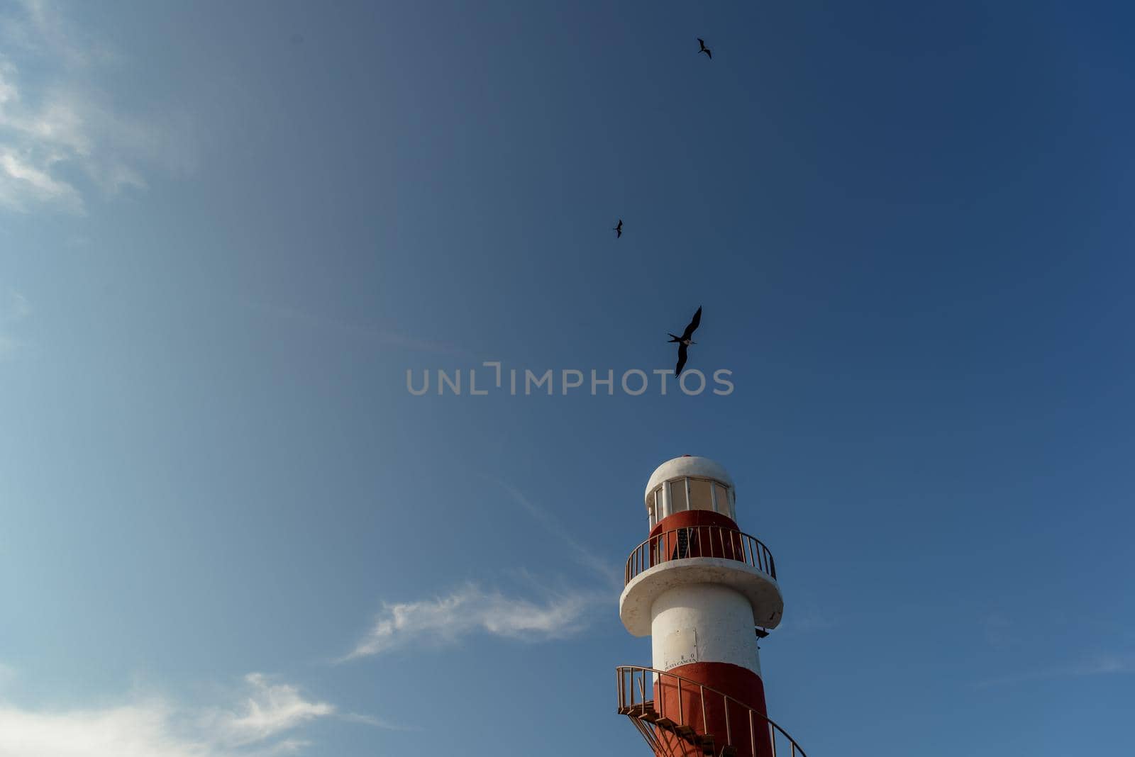 Top of a white-red lighthouse against a blue sky with an airplane. Mexico.