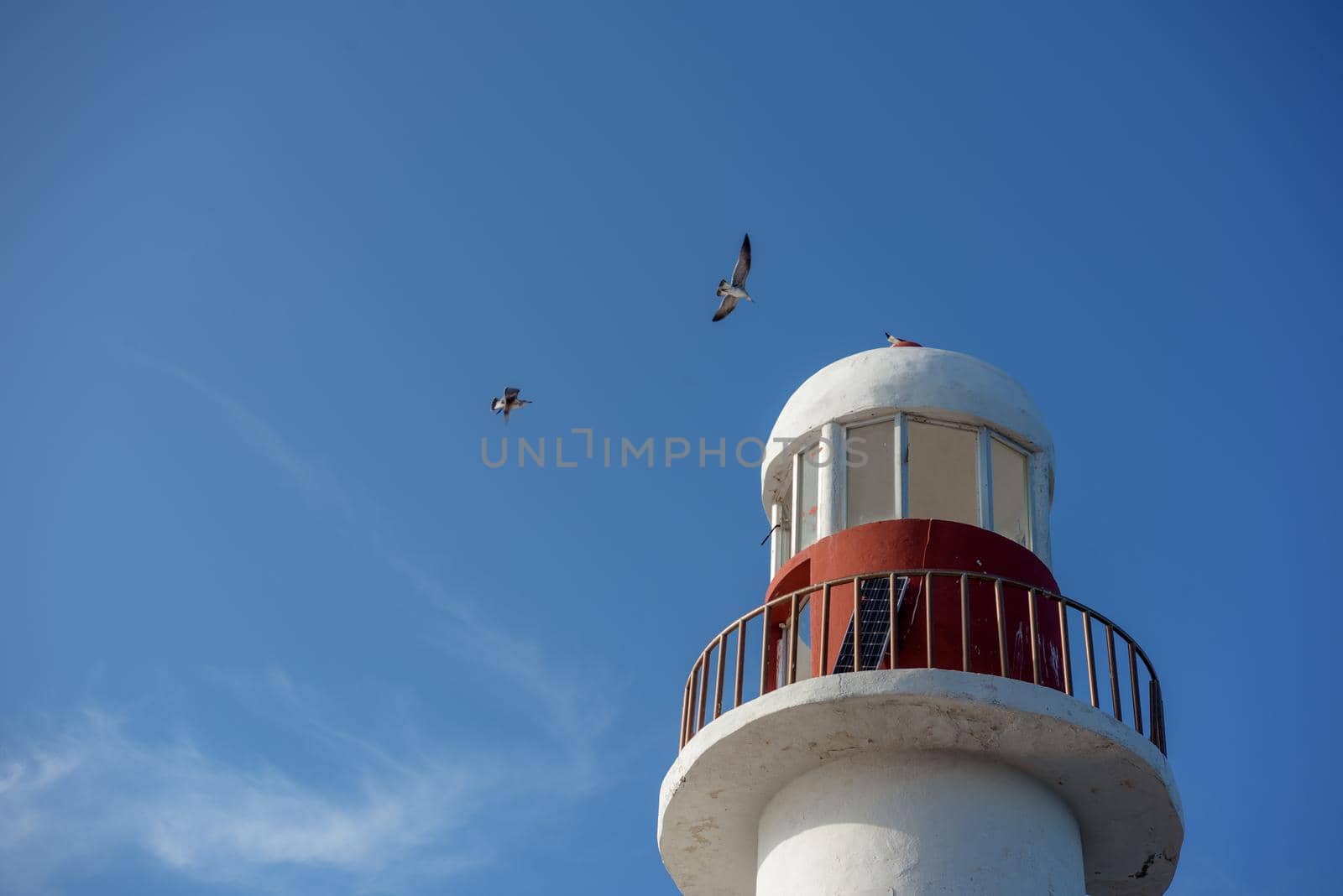 Top of a white-red lighthouse against a blue sky with an airplane. Mexico.