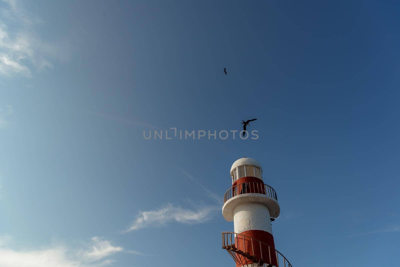 Top of a white-red lighthouse against a blue sky with an airplane. Mexico.