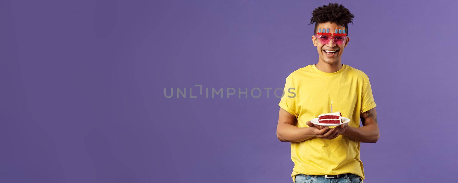 Celebration, party and holidays concept. Portrait of upbeat, charismatic lively man with dreads, hipster guy wearing funny glasses mask celebrating birthday, have fun, hold cake with candle by Benzoix