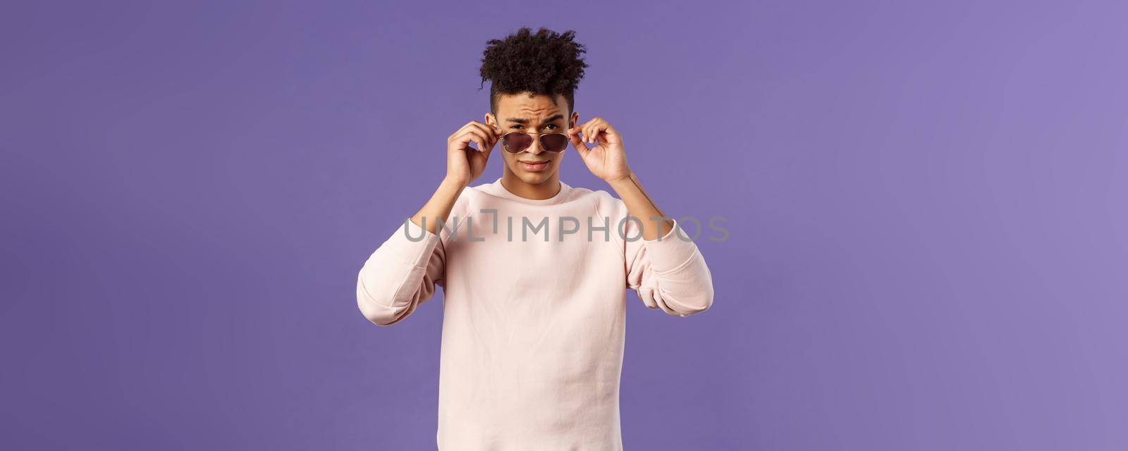 Portrait of sassy and confident young judgemental man, taking-off glasses squinting suspicious, security checking out and judging person near club door, standing purple background by Benzoix