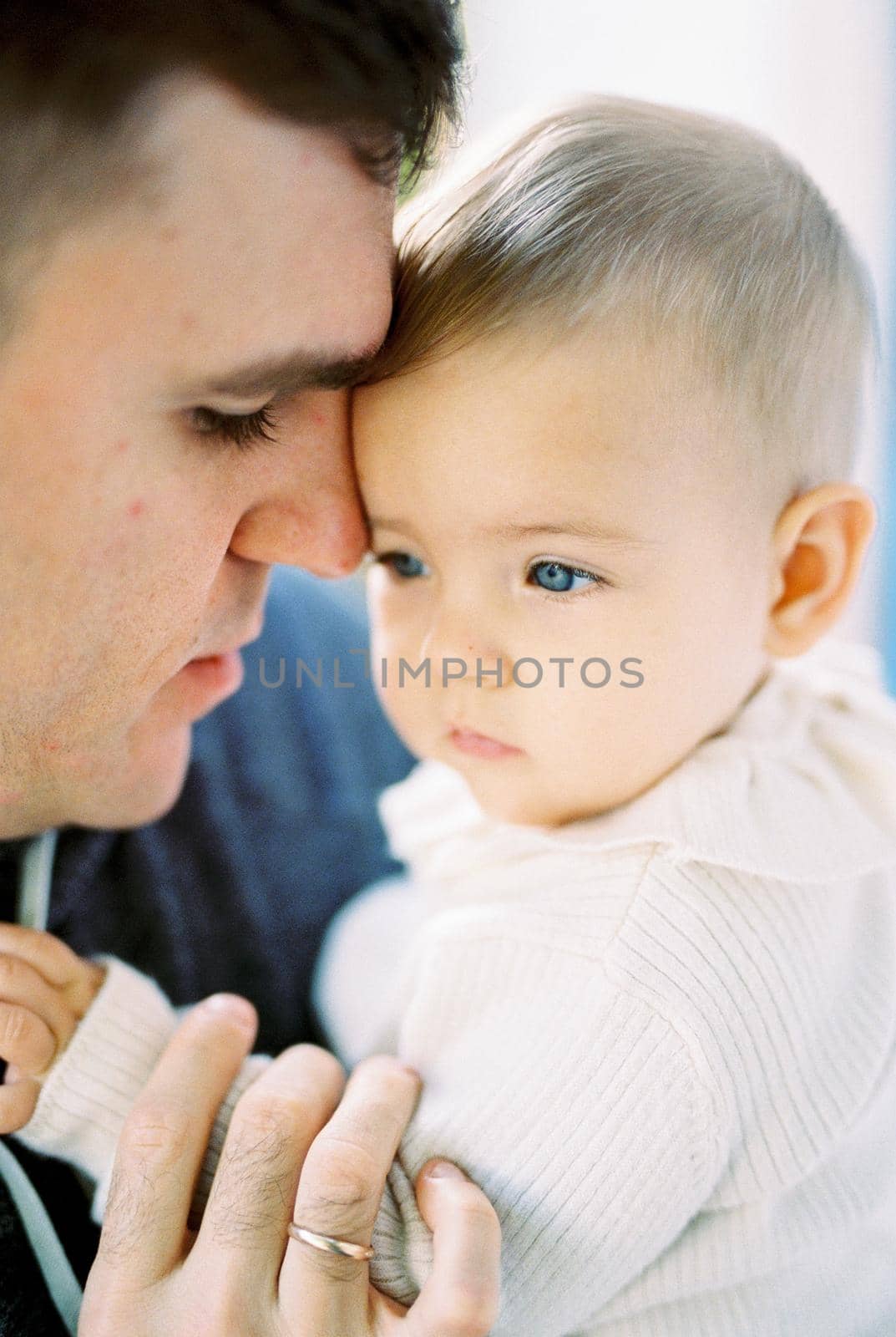 Dad touches the forehead of the baby with his nose, holding his hand with his fingers. Portrait by Nadtochiy