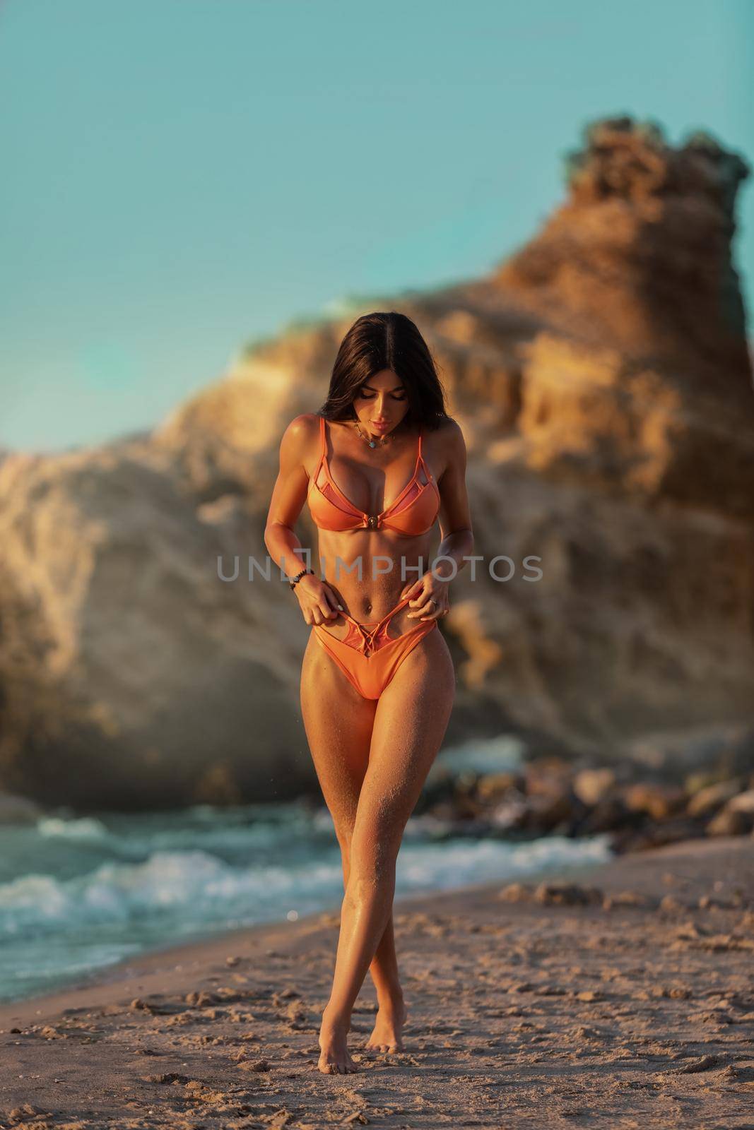 Beautiful athletic girl in a swimsuit walks along the seashore, strokes her hands along the body