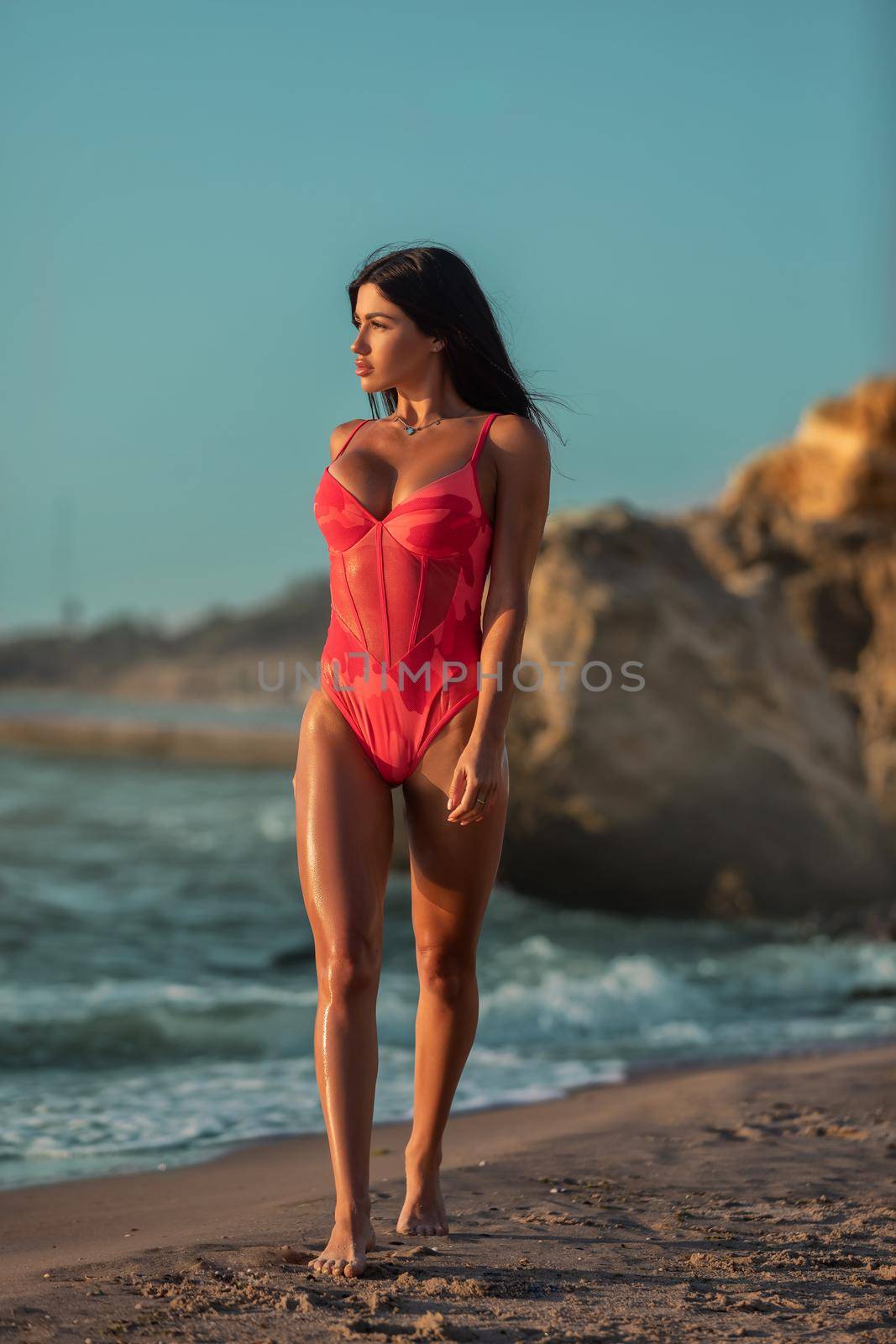 Tanned girl with perfect figure and silicone breasts walks along the seashore. by but_photo