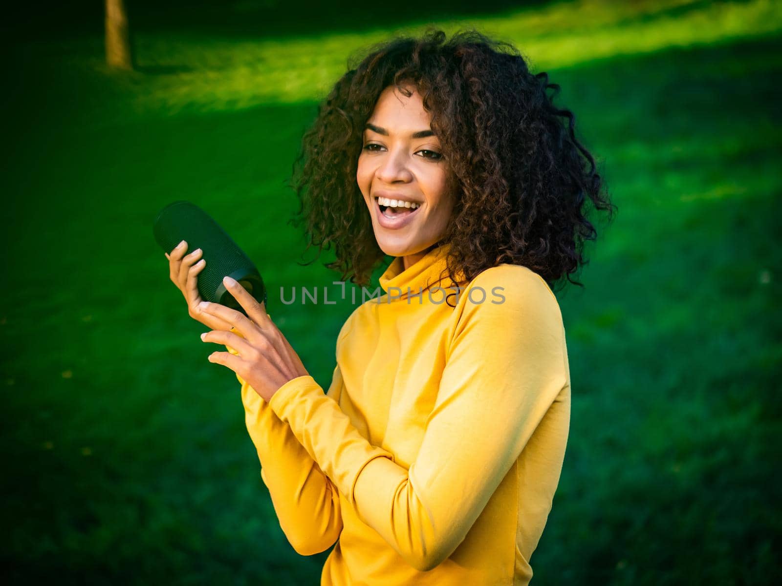 Modern trendy african american girl listening to music by wireless portable speaker.Young beautiful woman enjoying, dancing in park. by kristina_kokhanova