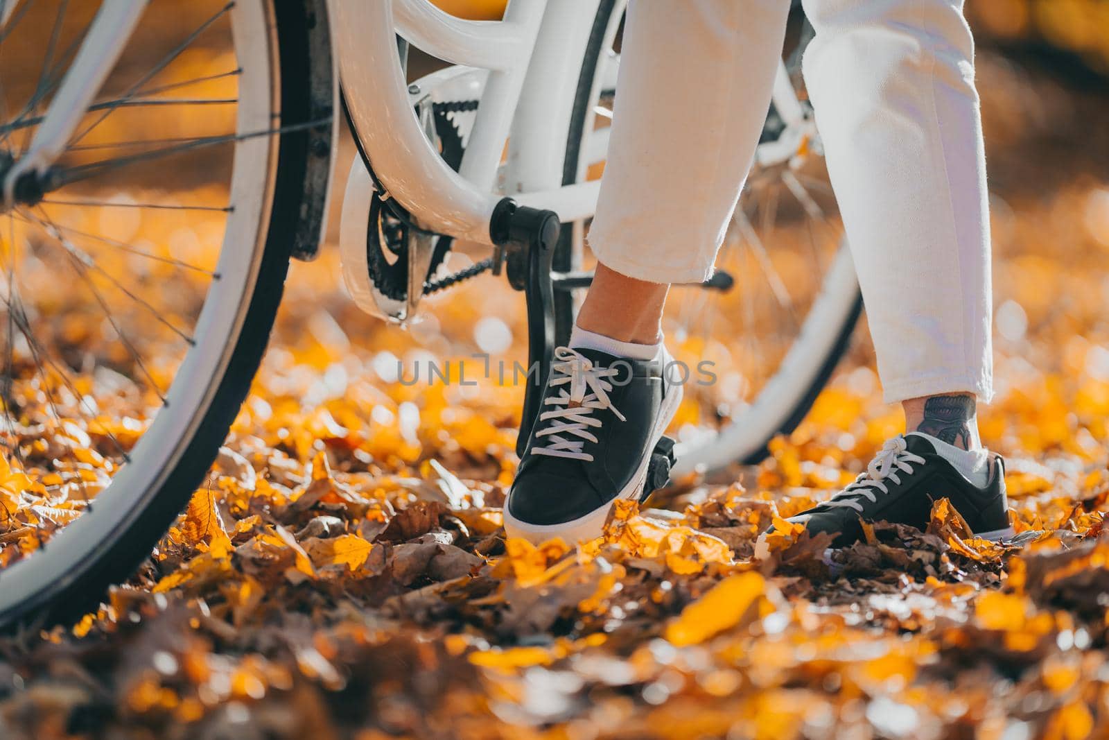 Close-up legs of woman in white pants cycling alone in autumn park. Sunny day, golden leaves in fall yellow forest. Unrecognizable girl on vintage bicycle,healthy lifestyle, aesthetic pic.High quality