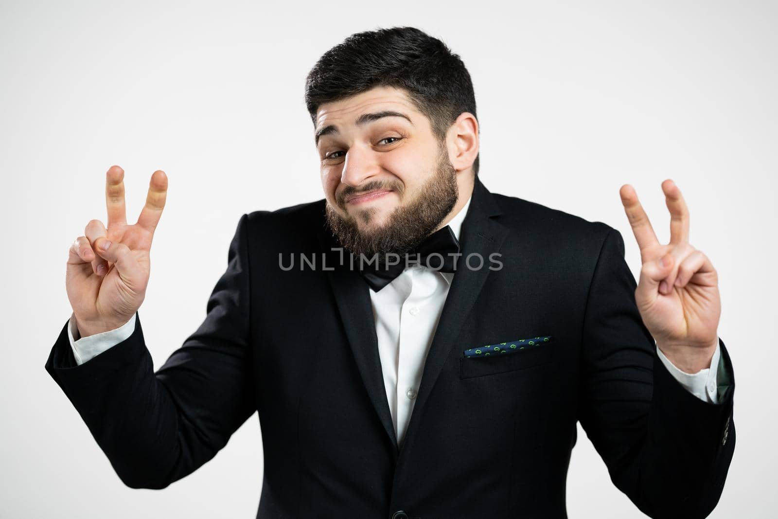 Handsome man showing with hands and two fingers air quotes gesture, bend fingers isolated on white background. Guy in black tuxedo. Not funny, irony and sarcasm concept. High quality photo