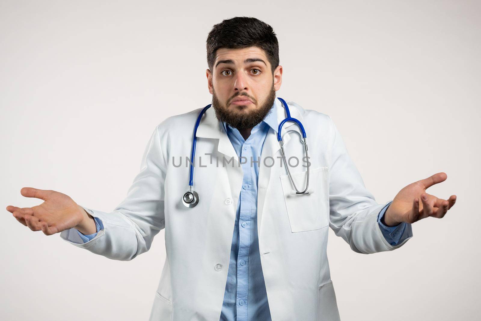 Unsure doctor man in medical coat shrugs his arms, makes gesture of I don't know, care, can't help anything .Doc on white background. High quality photo