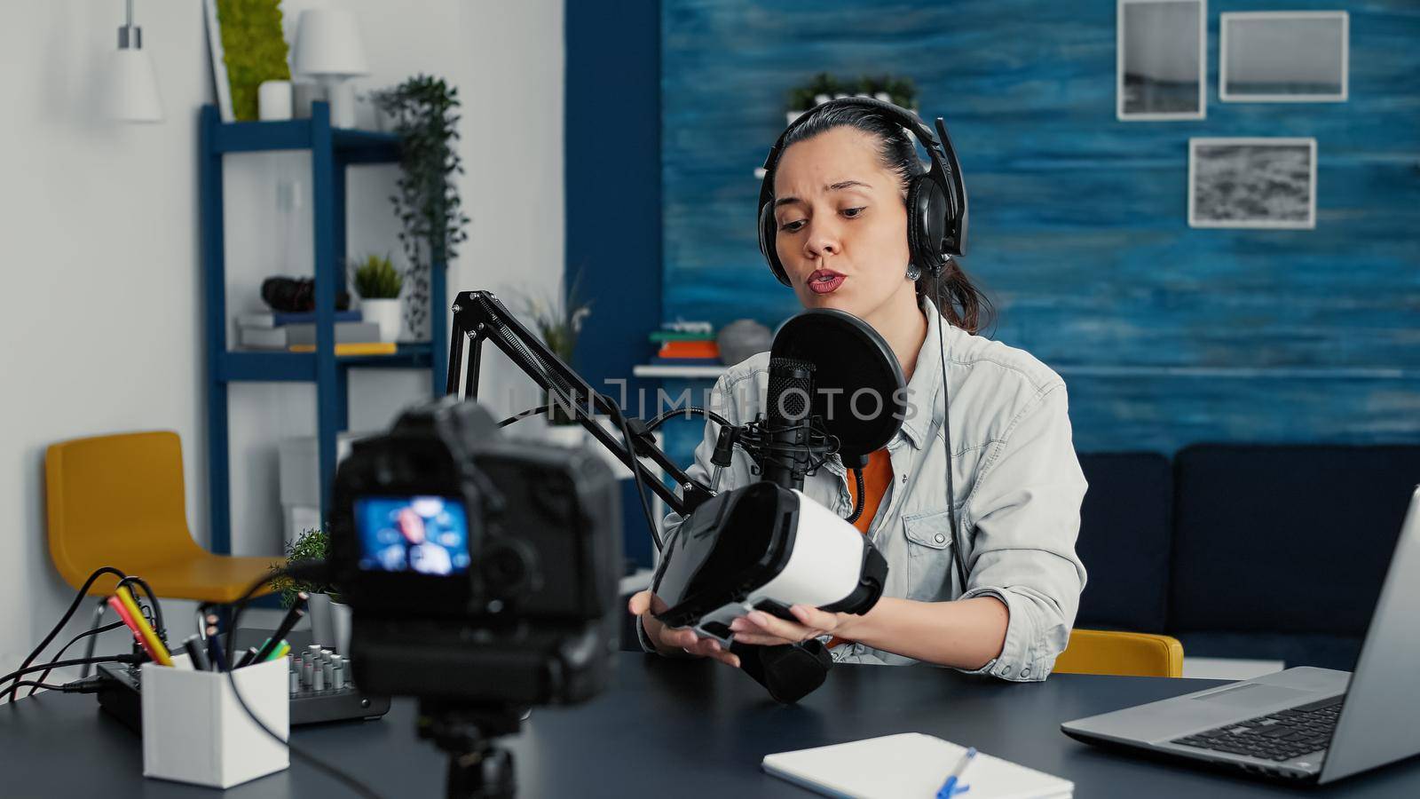 Tech enthusiast presenting VR wearable headset specifications to audience while recording video in living room studio. Vlogger sitting at desk while reviewing futuristic virtual reality goggles.