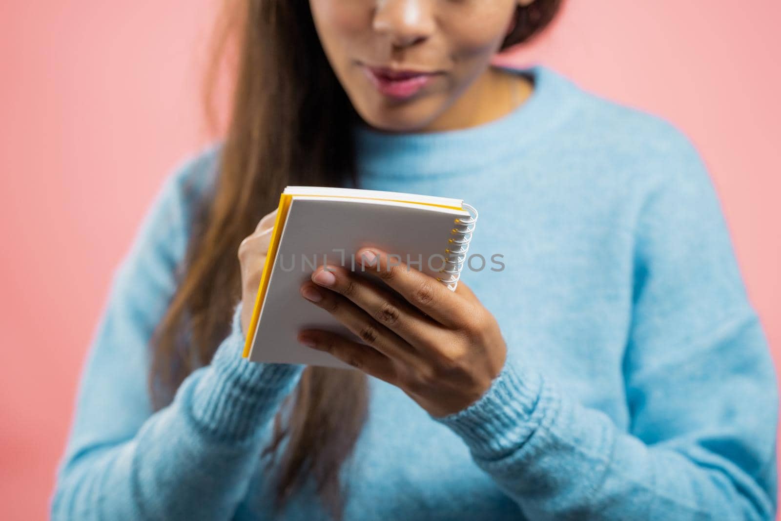 African woman making notes in planner, mature lady holding pen. She writes future plans and to-do list in notebook for week or month. Keeping personal diary on pink studio background