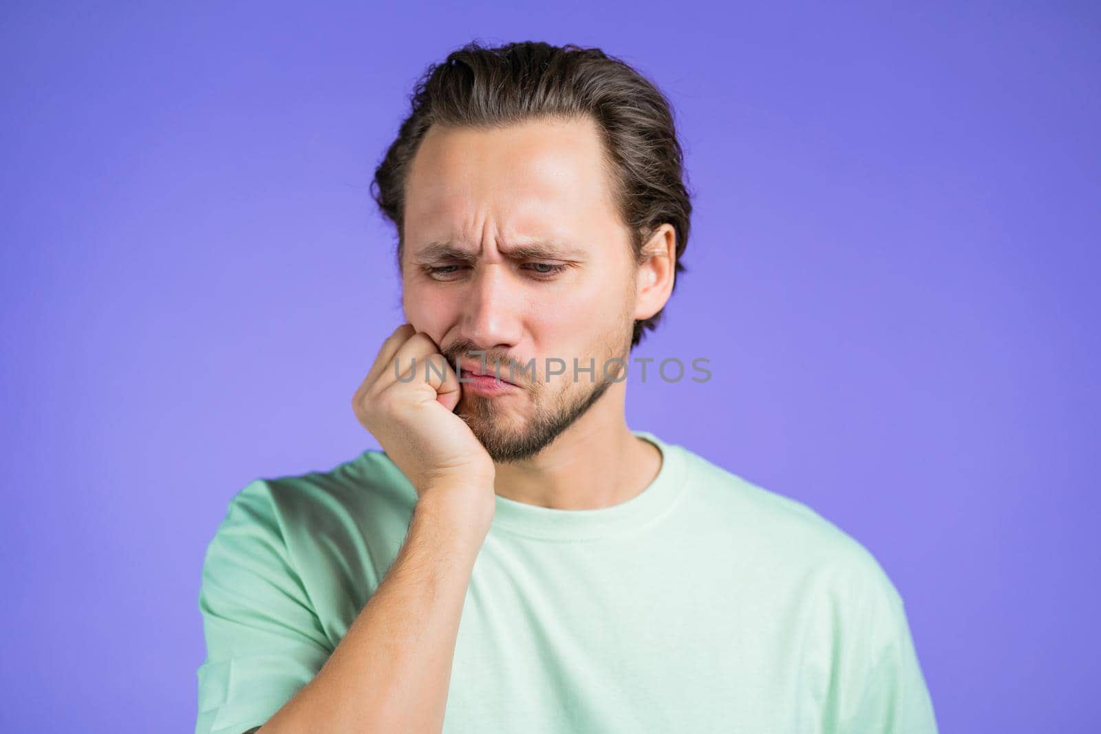 Young handsome man with tooth pain on violet studio background. Toothache, dental problems, stomatology and medicine concept. High quality photo