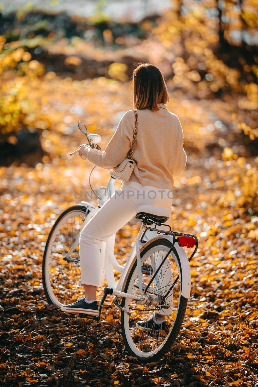 Beautiful portrait of woman cycling alone in autumn park. Sunny day, golden leaves in forest. Trendy lady on vintage white bicycle, healthy lifestyle, aesthetic scene. High quality photo