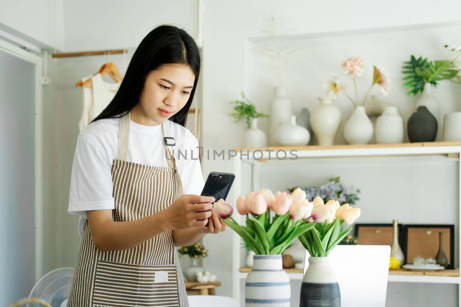 Happy asian female, small stock business owner holding phone product photography checking commercial shipping delivery order on smartphone using mobile app technology.