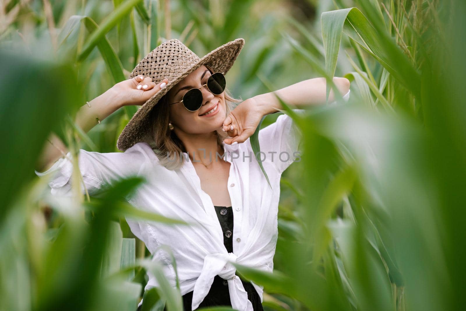 Portrait of young stylish woman in green jungle. Girl in straw hat and sunglasses, linen clothes. Lady looks happy and healthy, she smiles. High quality photo