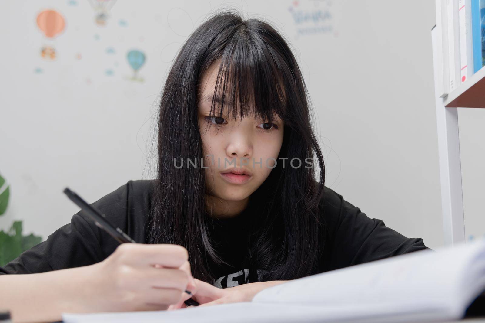 Asian student girl is writing homework and reading book at desk by aoo3771