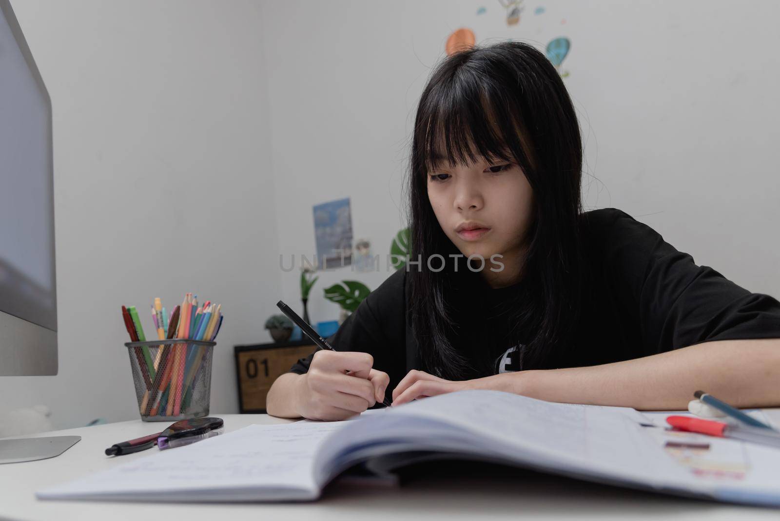 Asian student girl is writing homework and reading book at desk by aoo3771