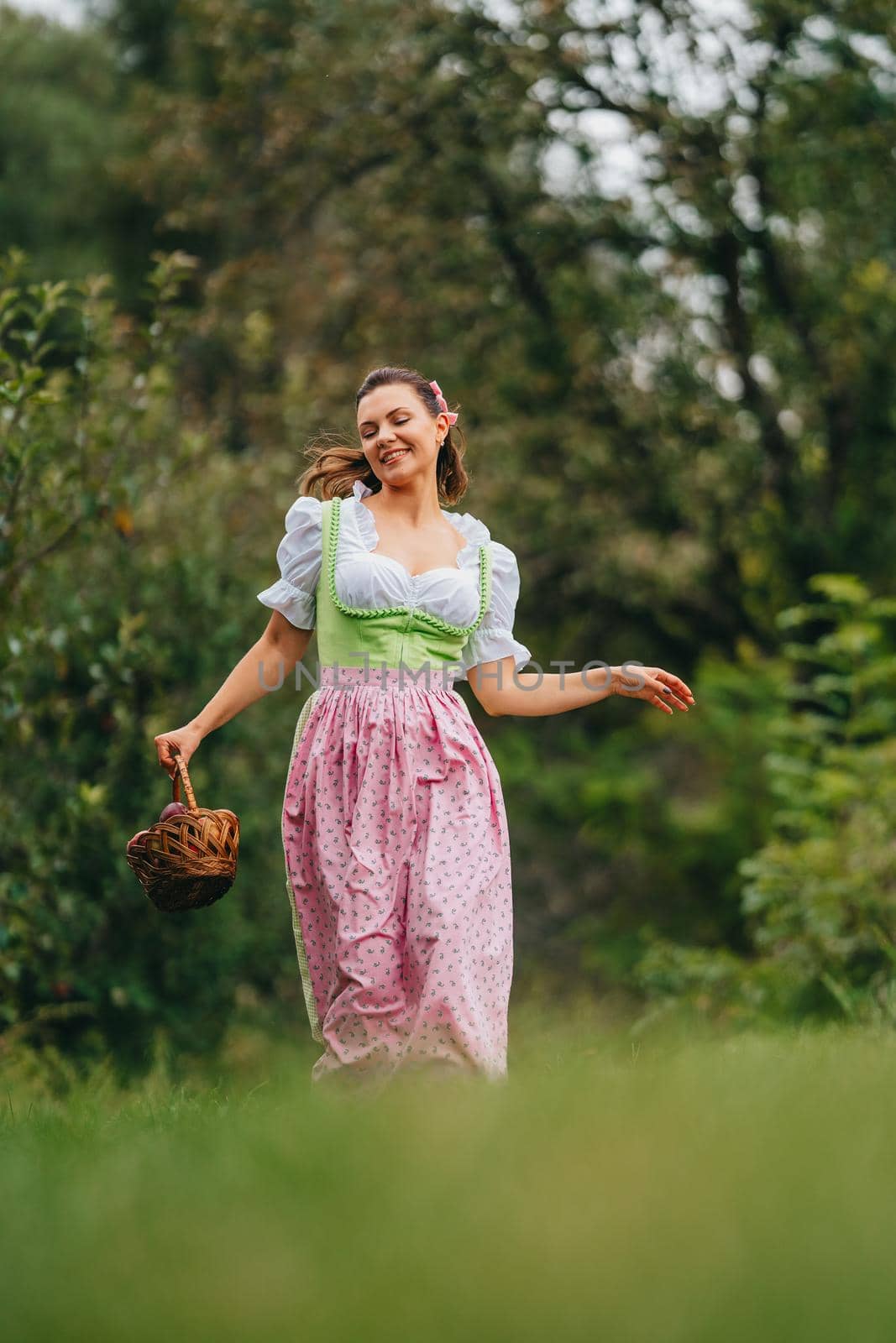 Pretty woman in dirndl - traditional festival dress running with basket in apple garden. Organic village lifestyle, agriculture, harvest, retro style concept. High quality photo