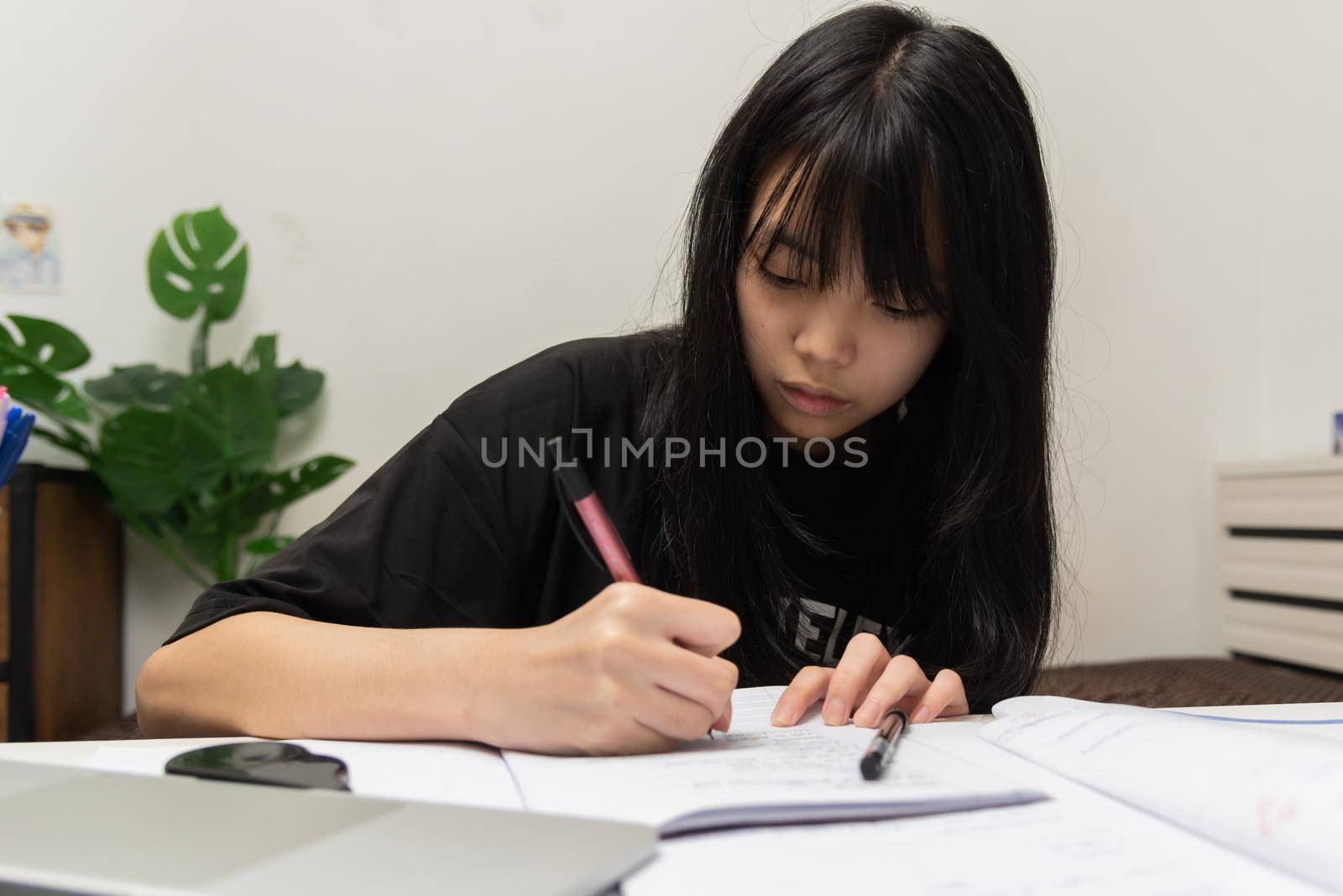 Asian student girl is writing homework and reading book at desk by aoo3771