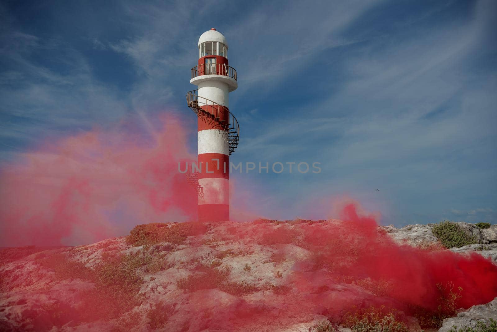 A lighthouse on a rocky coast in Cancun with a red smoke screen.