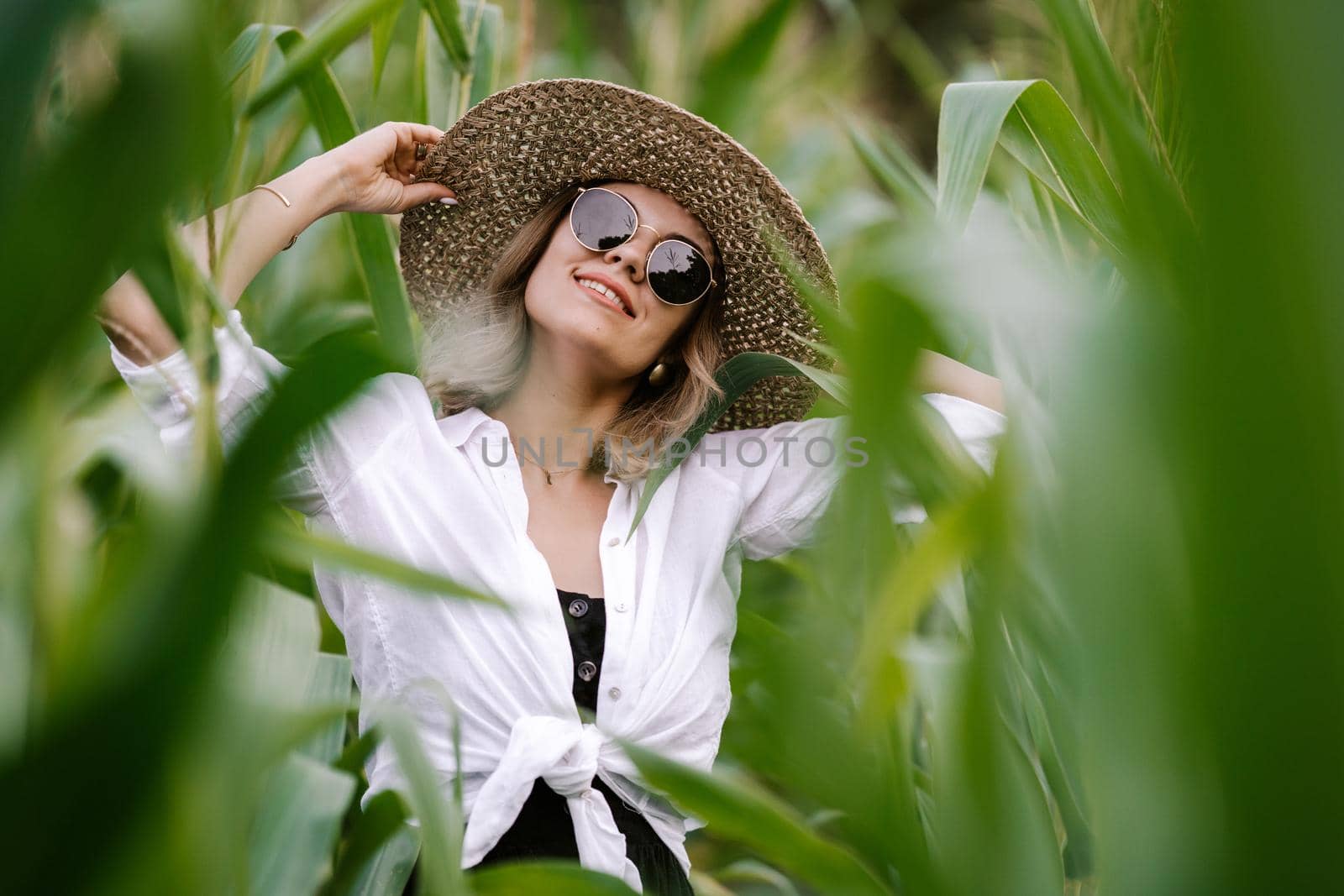 Portrait of young stylish woman in green jungle. Girl in straw hat and sunglasses, linen clothes. Lady looks happy and healthy, she smiles. High quality photo