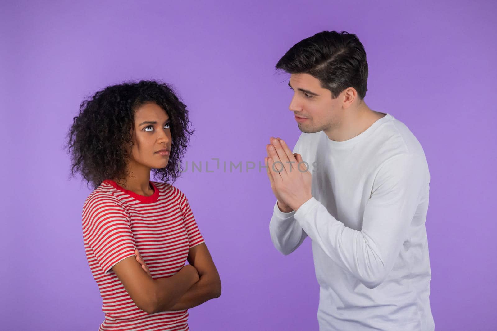 Young man begging his girlfriend or wife about something over purple background. Guy want his african woman to satisfy desires, help with. interracial couple. High quality photo