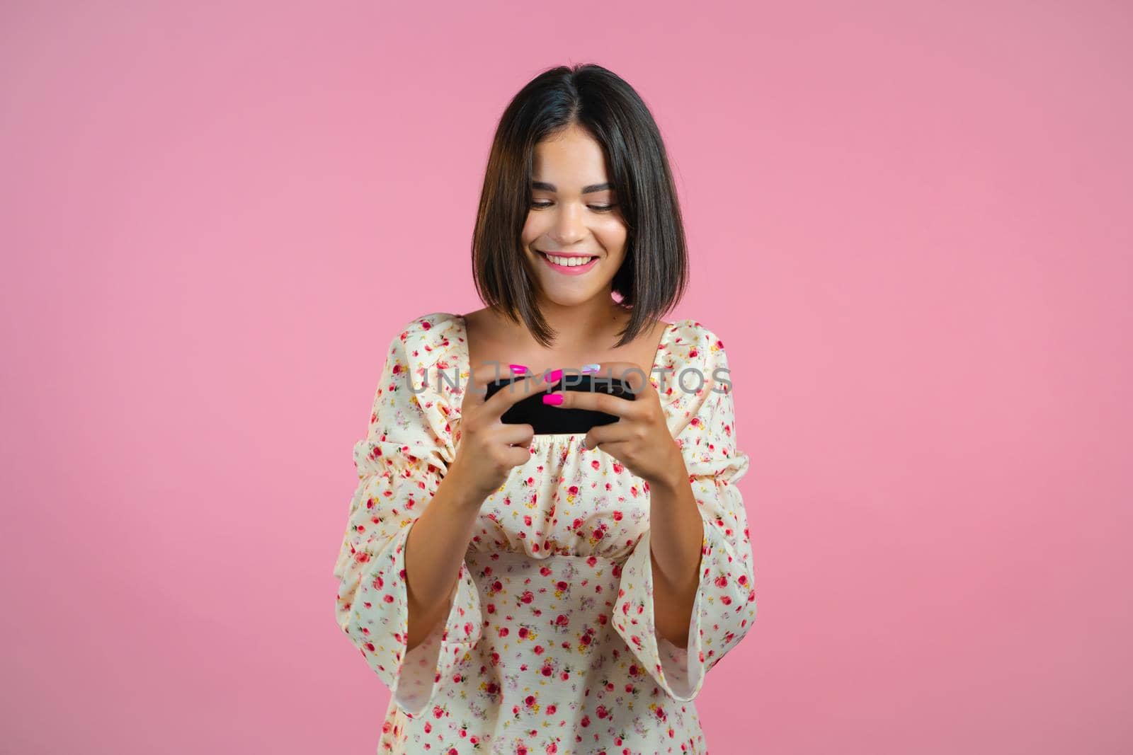 Woman playing game on smartphone on pink studio wall. Using modern technology - apps, social networks. by kristina_kokhanova