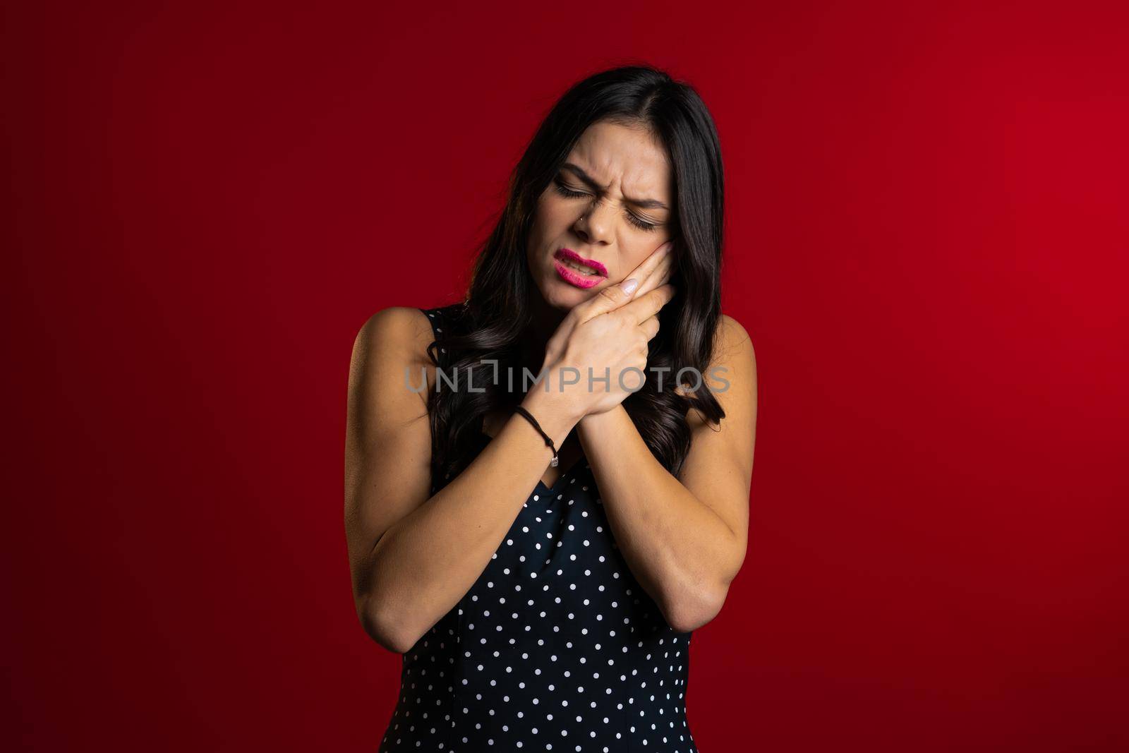 Young pretty latin woman with tooth pain on red studio background. Toothache, dental problems, stomatology and medicine concept