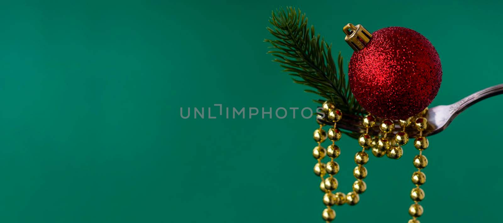 banner with Close up of Christmas decorations on a fork of gold beads, a branch of a Christmas tree and a red Christmas ball on a green background. concept for chinese or oriental new year. by Leoschka