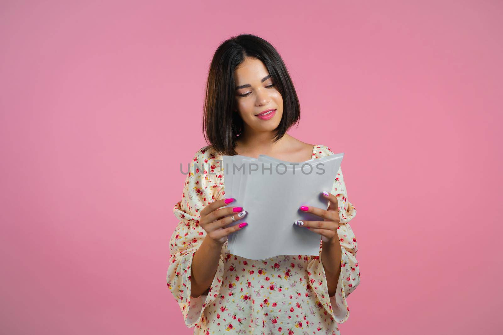Satisfied woman in floral dress holding files papers isolated on pink background. Pretty girl checks documents, utility bills. by kristina_kokhanova