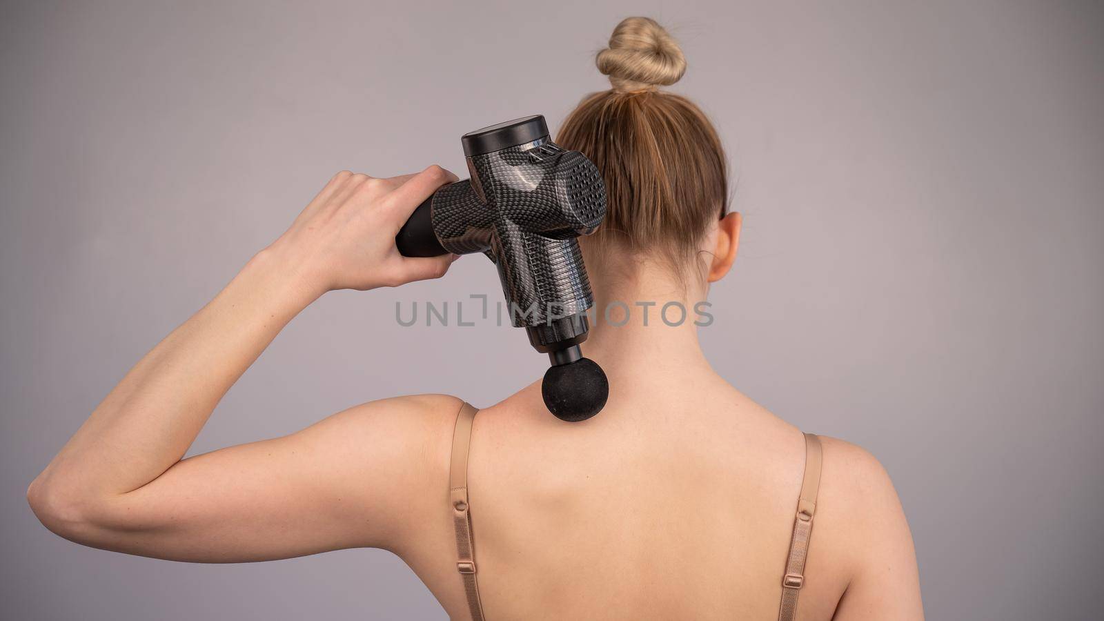 Caucasian woman giving herself a back massage with a gun