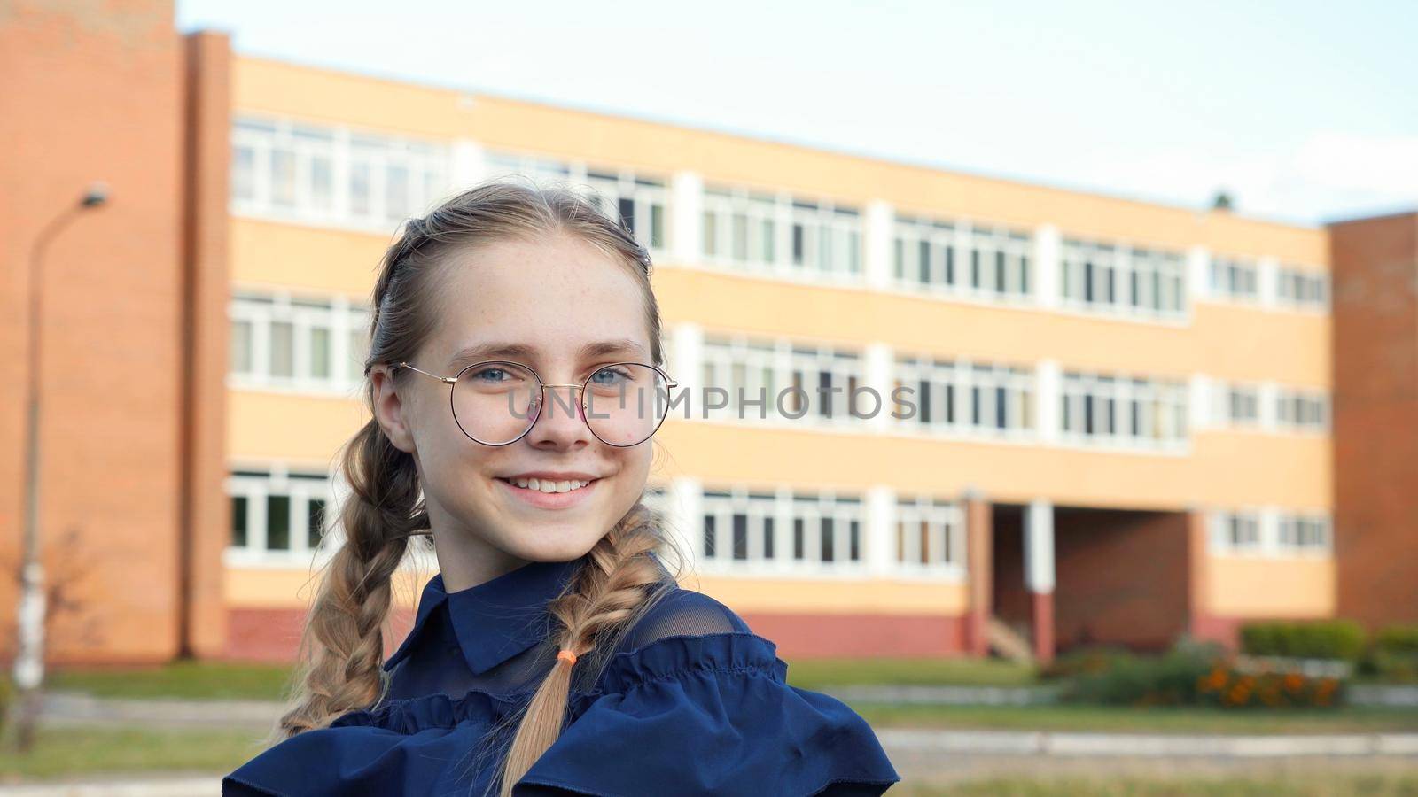 A teenage girl wearing glasses in front of a school