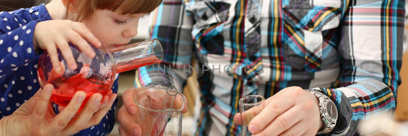 Man and little girl are playing colorful liquids in flasks. Research equipment with color reagent or food additives at home concept
