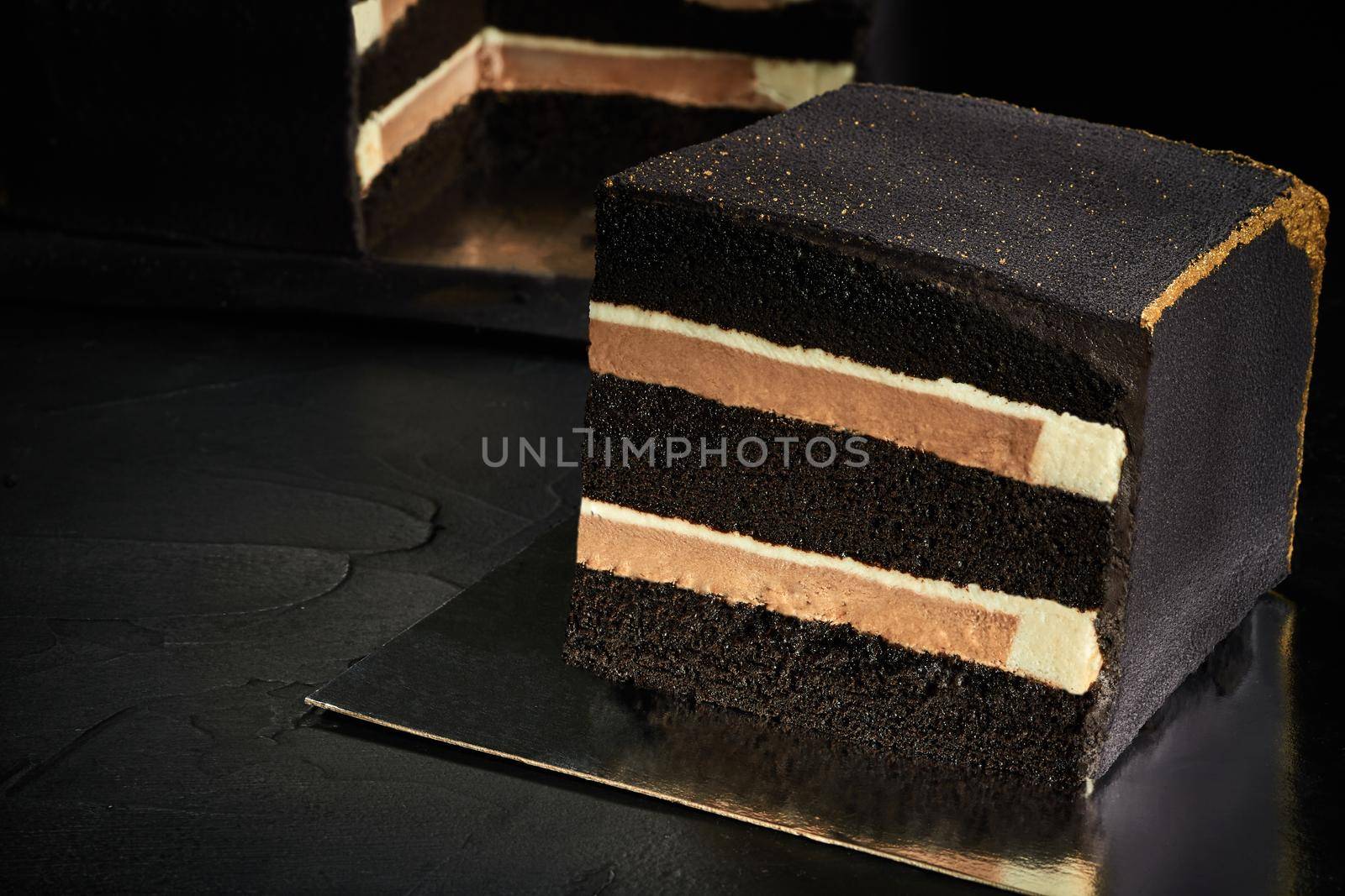 Black square cake with gold edges. Dark background. The view from the top. Confectionery art