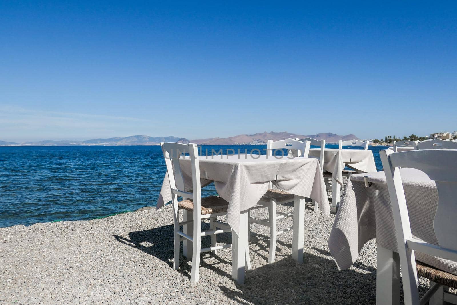 White restaurant tables on the beach in summer - travel, vacation and summer concept. The perfect lunch with a sea view