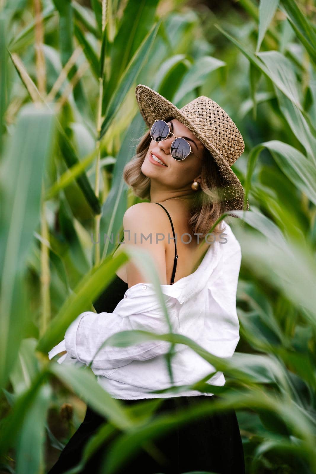 Portrait of young stylish woman in green jungle. Girl in straw hat and sunglasses, linen clothes. Lady looks happy and healthy, she smiles. High quality photo