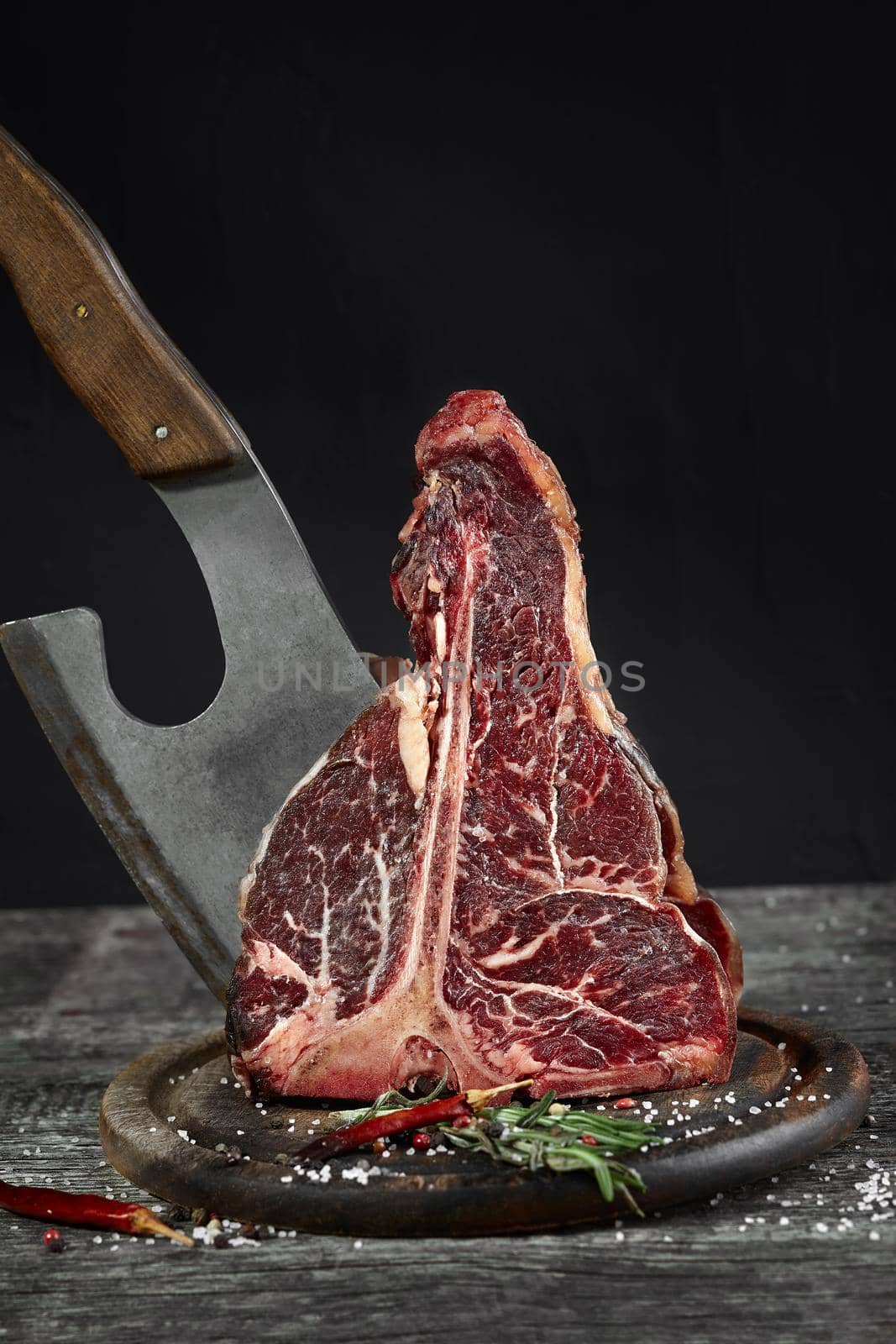 Fresh raw t-bones steak on an olive wooden board with sea salt and a kitchen ax. Copy space.