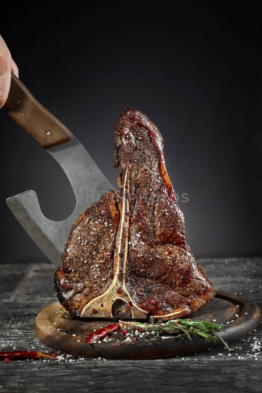 Grilled T-Bone Steak with salt,pepper and a kitchen ax on cutting board on dark background. Copy space.