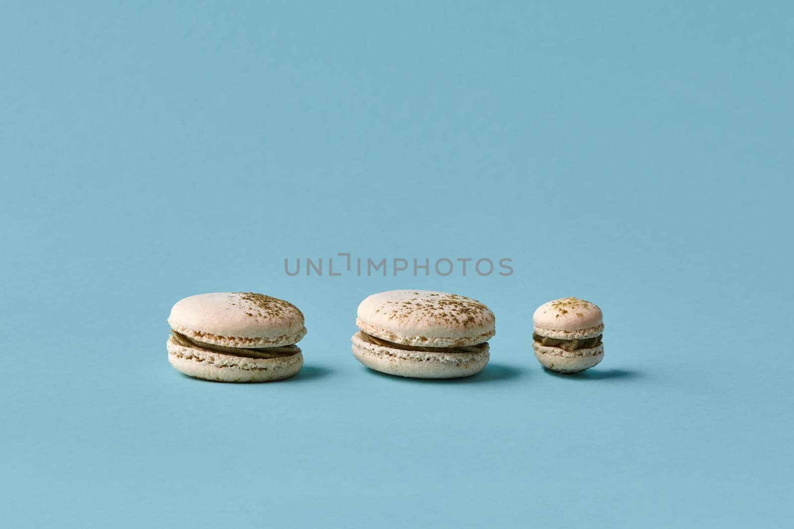 White macarons cake with colorful powder, top view, flat lay, sweet macaroon on blue background. Minimal concepts macaroons pattern above, food background. Different size cookies