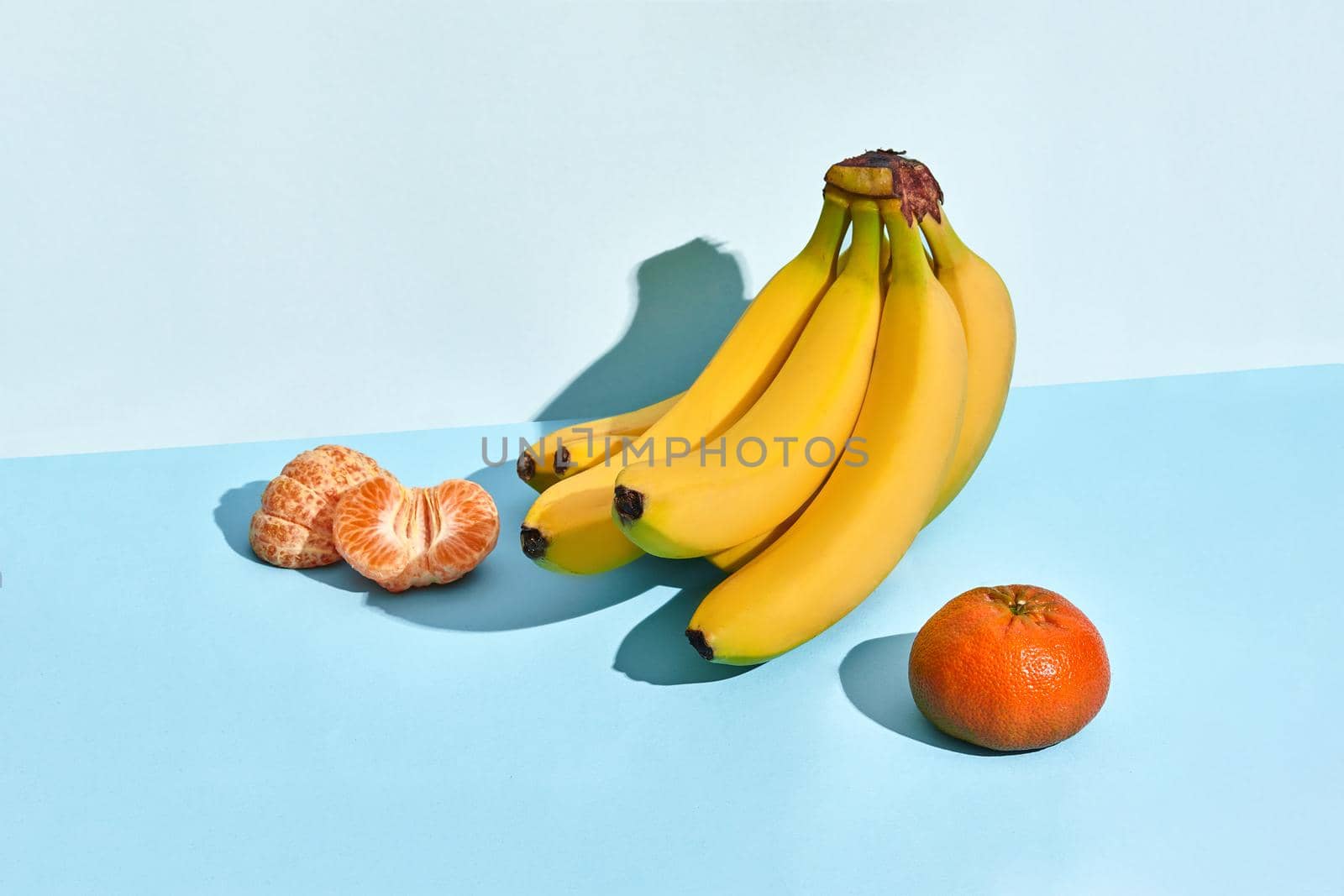 Composition of fresh fruits, banana and mandarin, half of peeled mandarin on blue background. Mock up, two-colored pastel