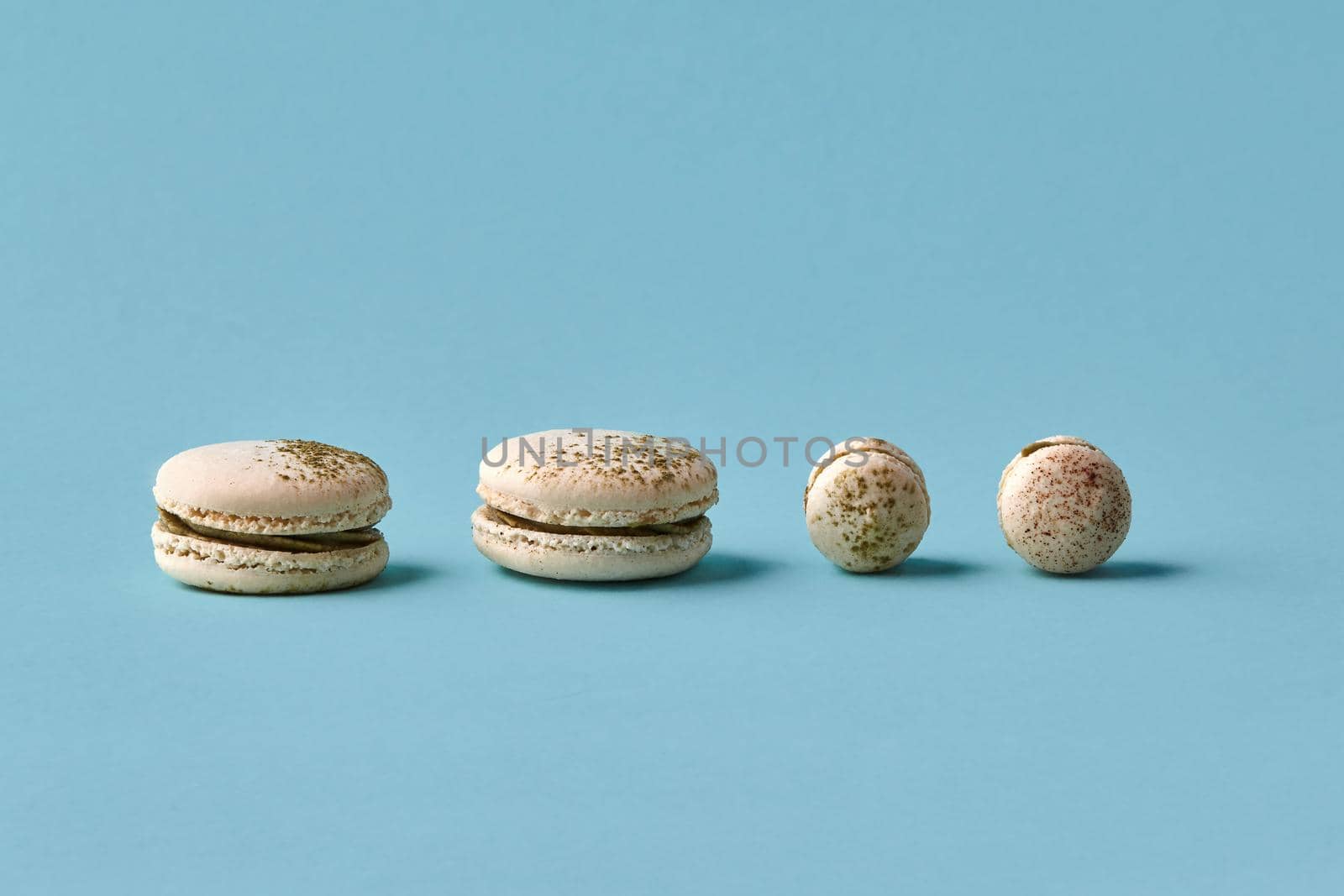 White macarons cake with colorful powder, top view, flat lay, sweet macaroon on blue background. Minimal concepts macaroons pattern above, food background. Different size cookies