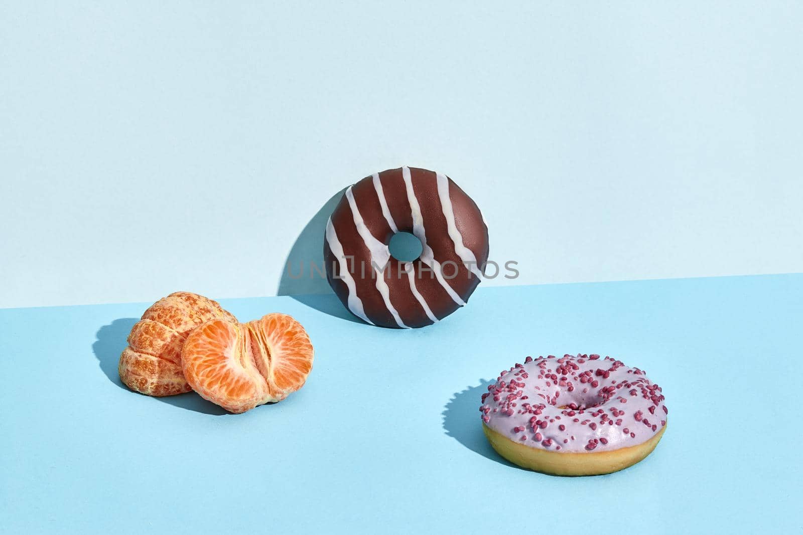 Composition of fresh fruits and sweets, two donuts and mandarin, half of peeled mandarin on blue background. Mock up, two-colored pastel