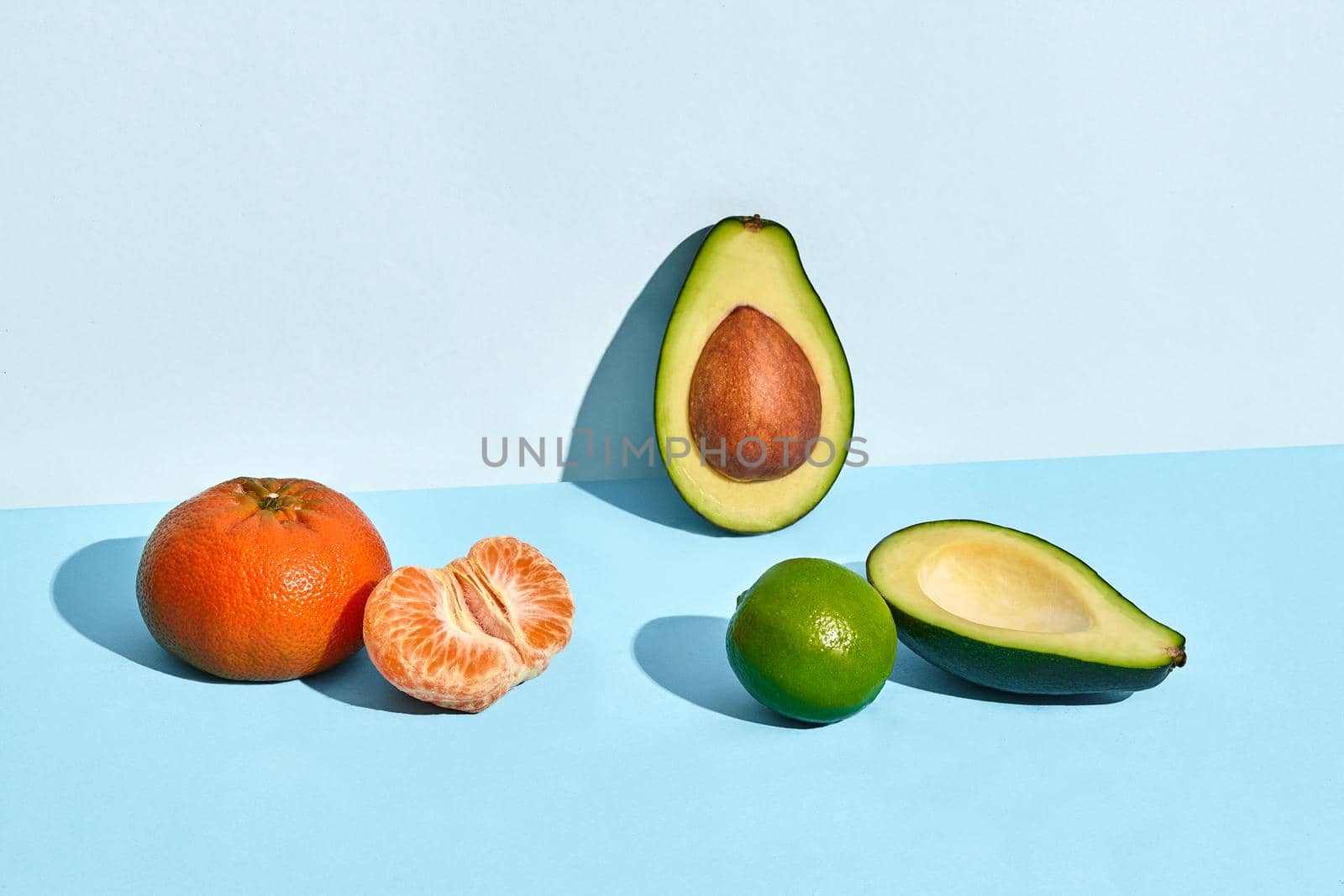 Composition of fresh fruits, mandarin lime and two halfs of cutted avocado on two-colored background by nazarovsergey