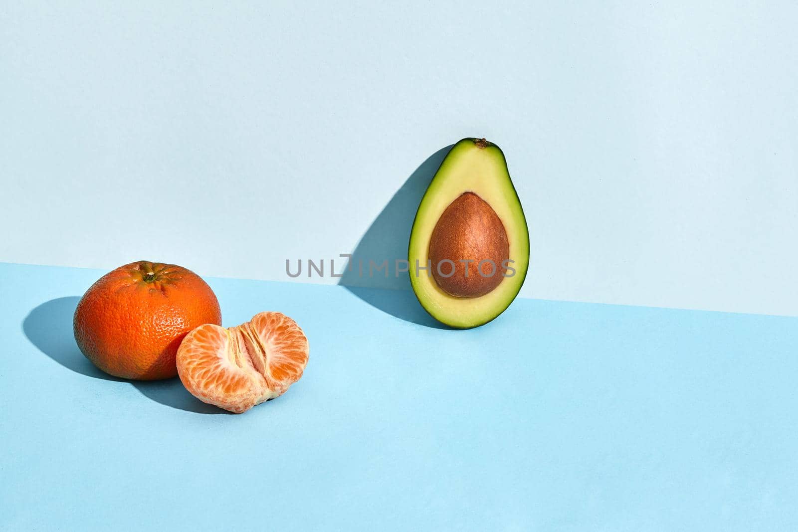 Composition of fresh fruits, mandarin and half of cutted avocado on blue background. Mock up, two-colored pastel