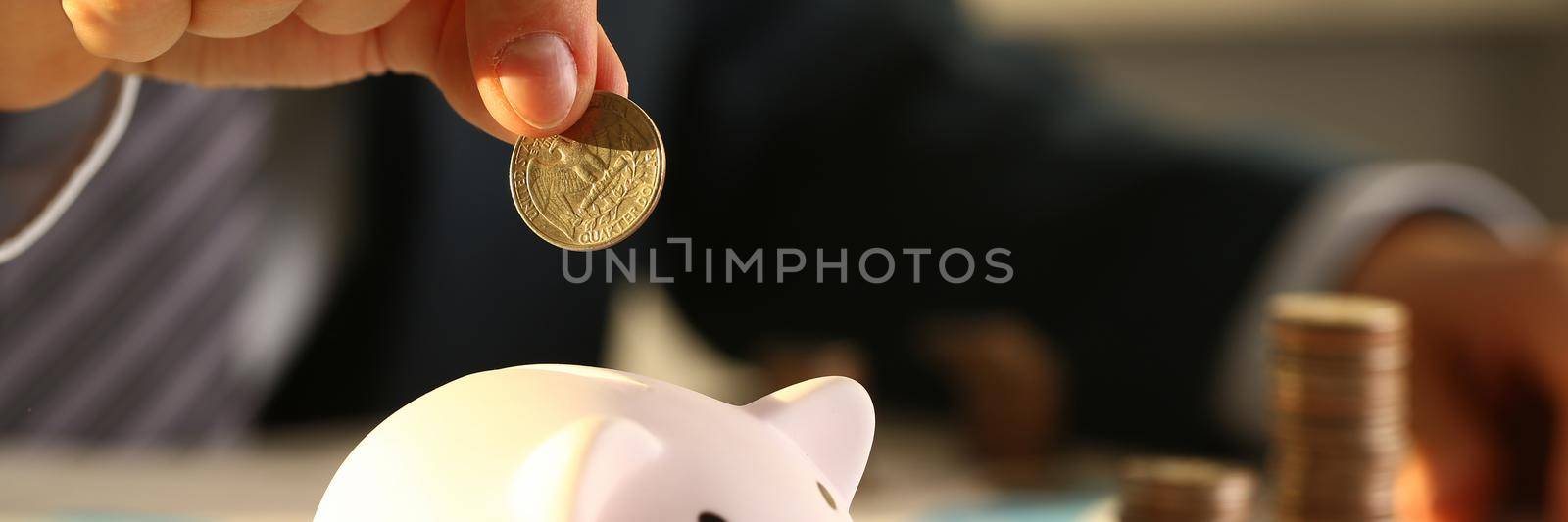 Businessman hand throws a coin into piggy bank by kuprevich