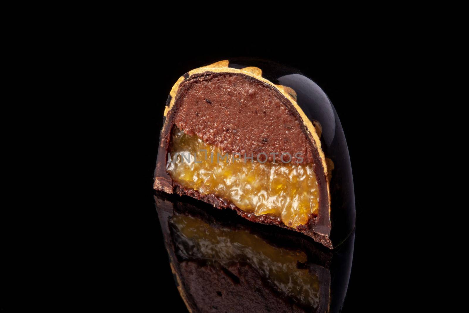Cut luxury handmade candy with chocolate and yellow confiture filling on black background. by nazarovsergey
